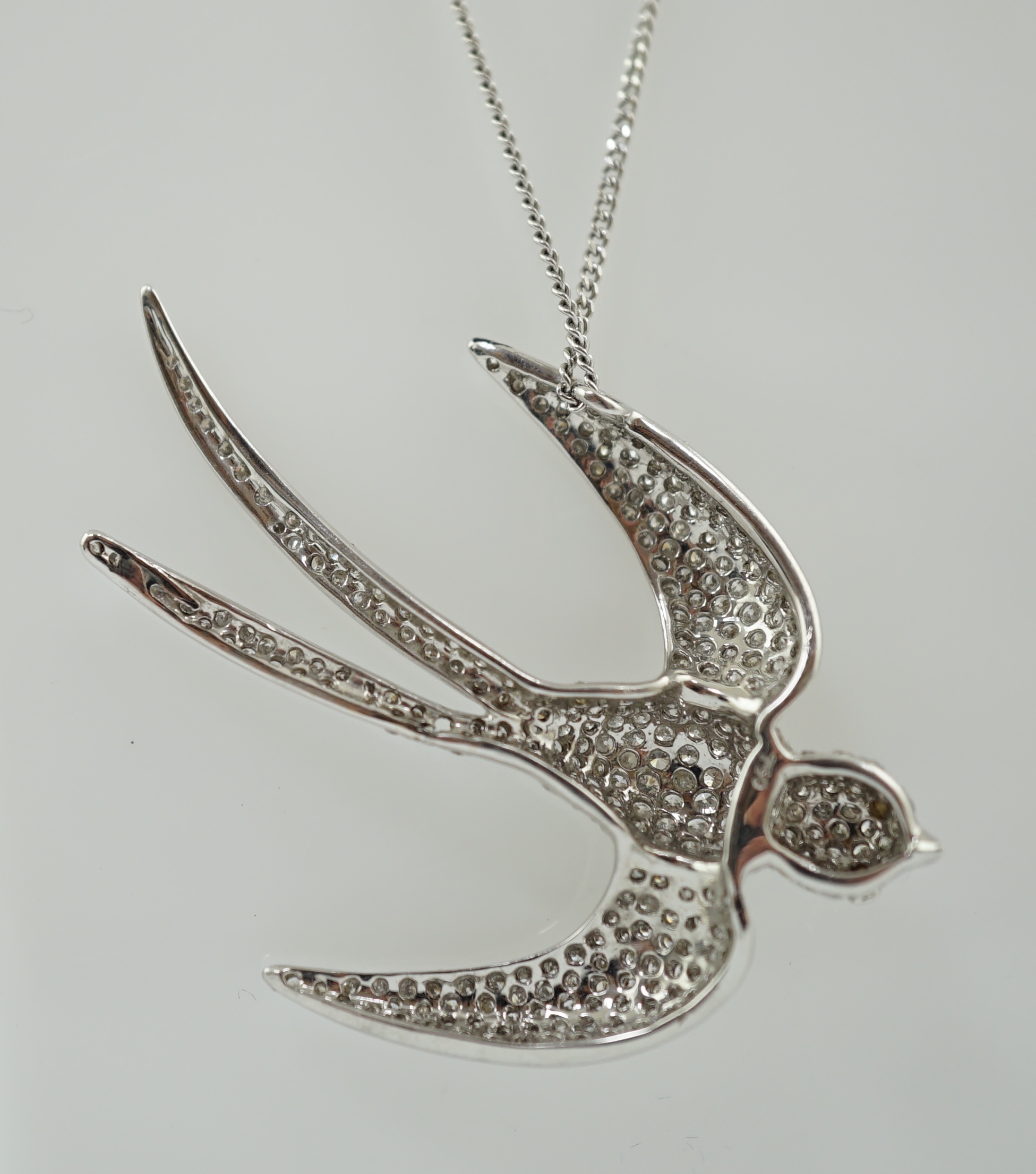 A modern 18k white gold and pavé set diamond pendant, modelled as a swallow, on an 18ct white gold fine link chain